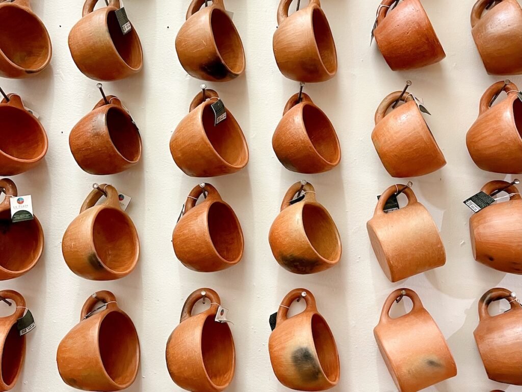 white wall with rows of brownish clay coffee mugs hanging from the handle