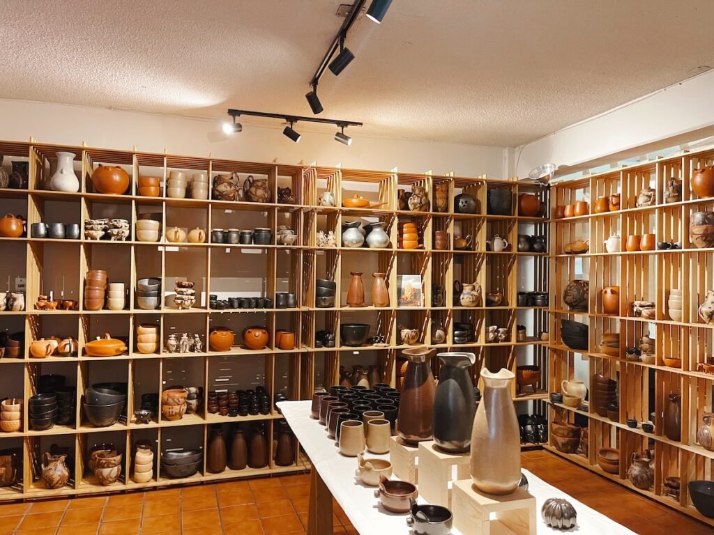 pottery of all shapes and sizes in display on wooden cubicle trays in the background. There's a table with clay ceramics in the foreground