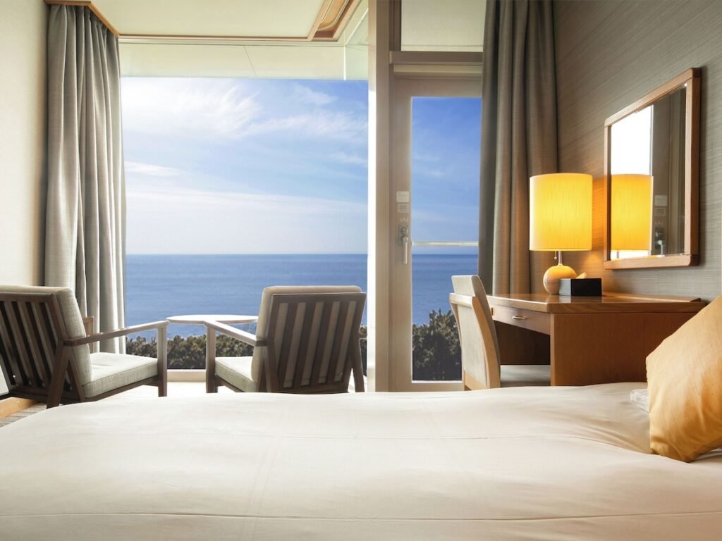 Kamakura Prince hotel room picturing half a bed and two chairs facing the floor to ceiling windows view to the ocean